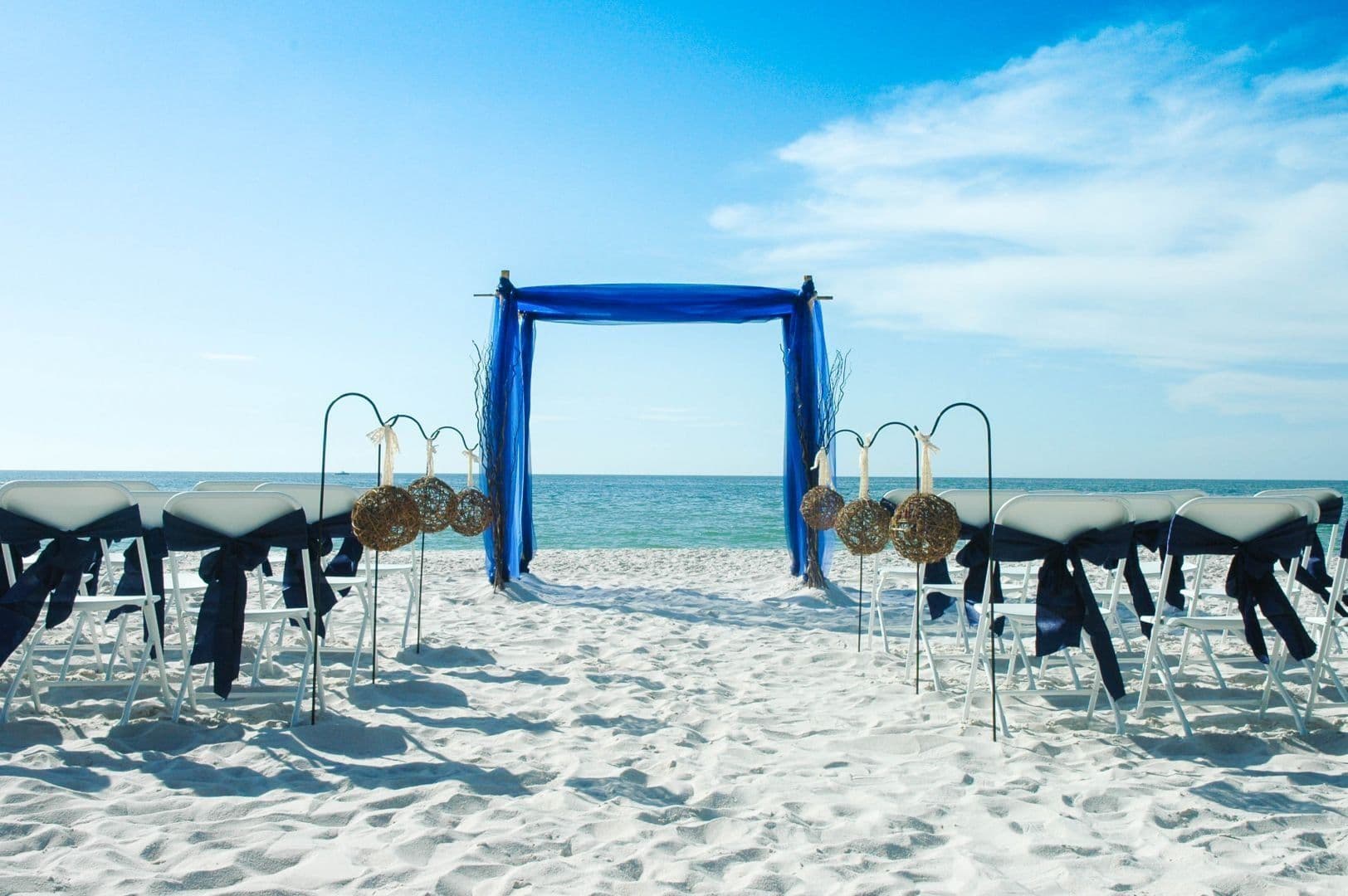 Beach wedding setup with blue arch and chairs facing the ocean.