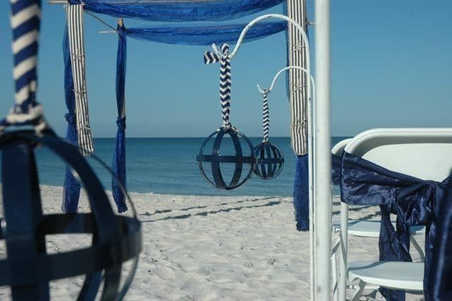 Beach wedding setup with blue decor, white chairs, and ocean view.