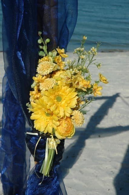 Yellow flowers tied to a blue draped pole on a beach.