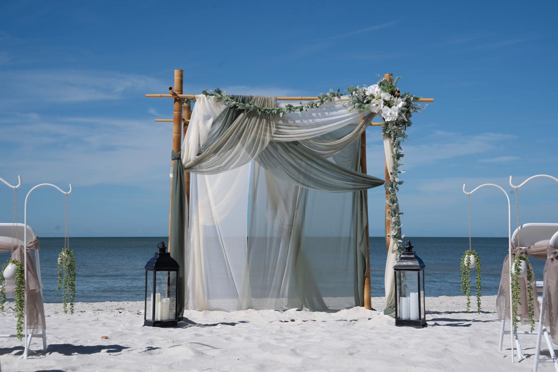 Four-post canopy setup with sage and white fabric draping and ocean backdrop