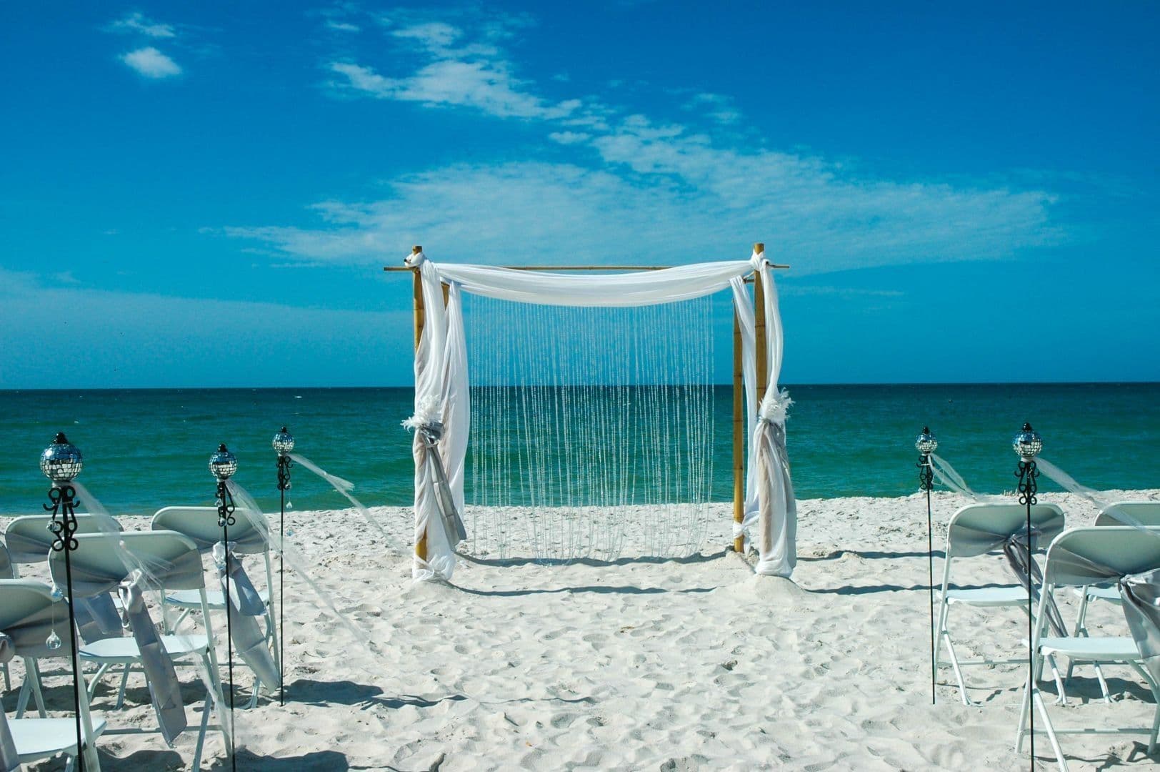 Beach wedding setup with white chairs, arch, and ocean backdrop.