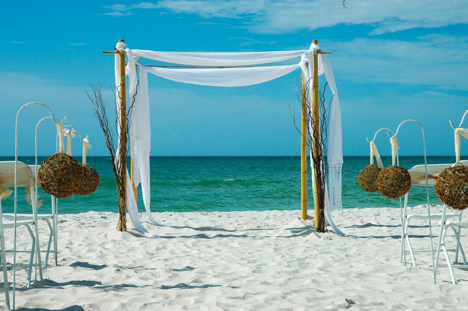 Four-post bamboo canopy with white draping and ocean backdrop