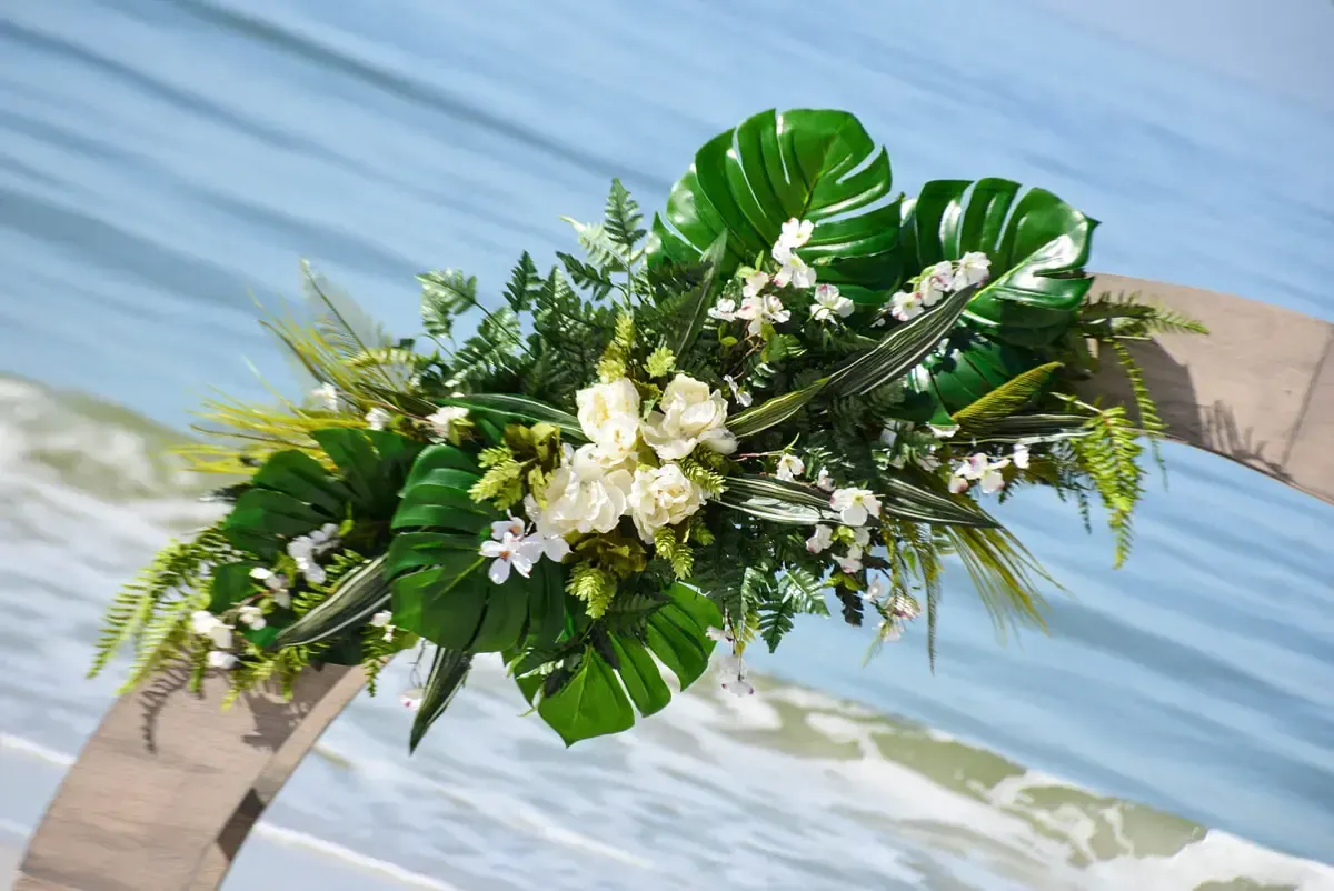 Tropical floral arrangement on arch with ocean background.