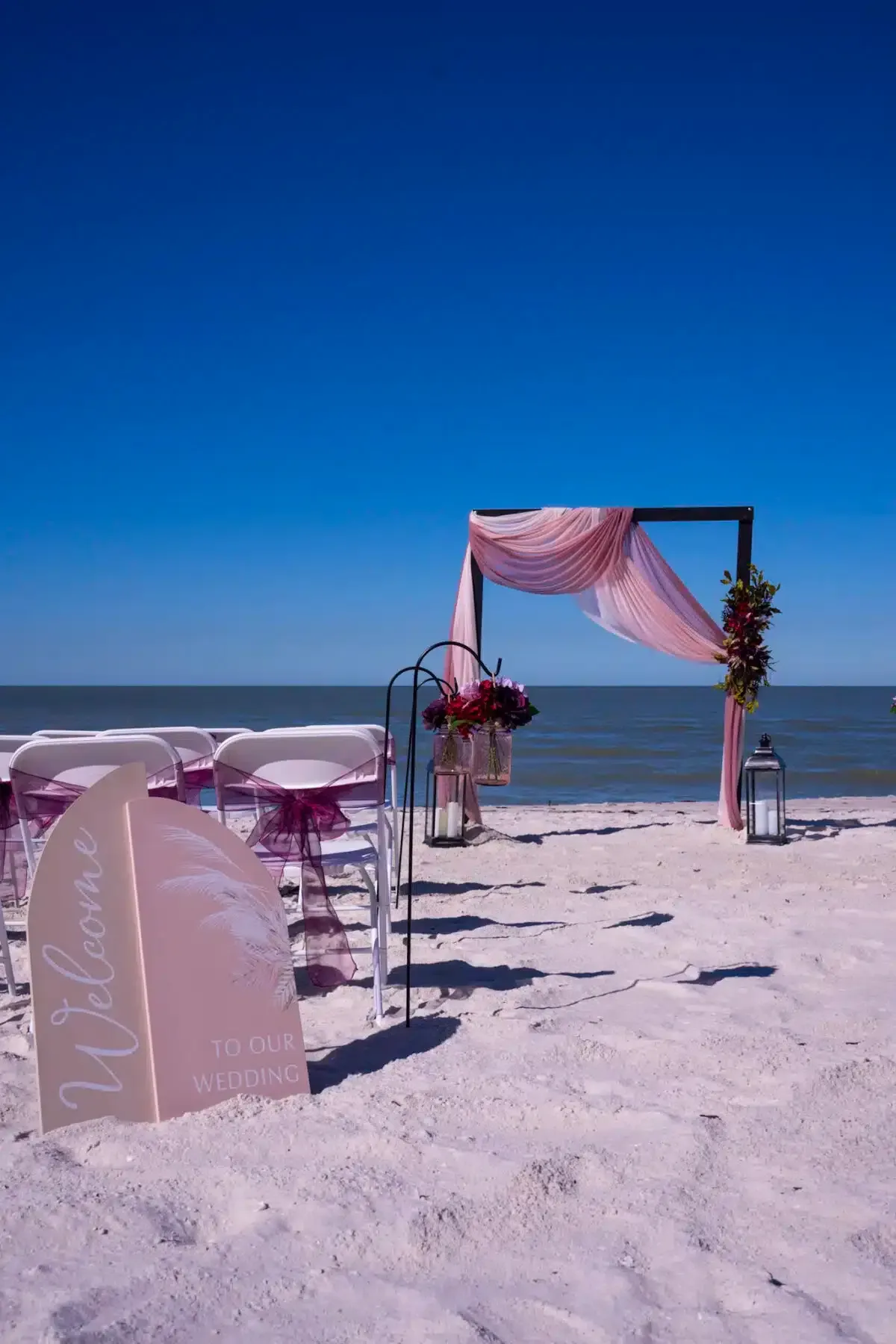 Wedding ceremony setup on a sunny beach with archway, chairs, and