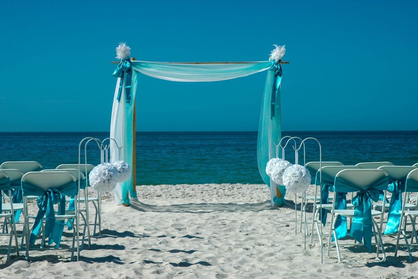 Beach wedding setup with turquoise decorations and ocean backdrop.