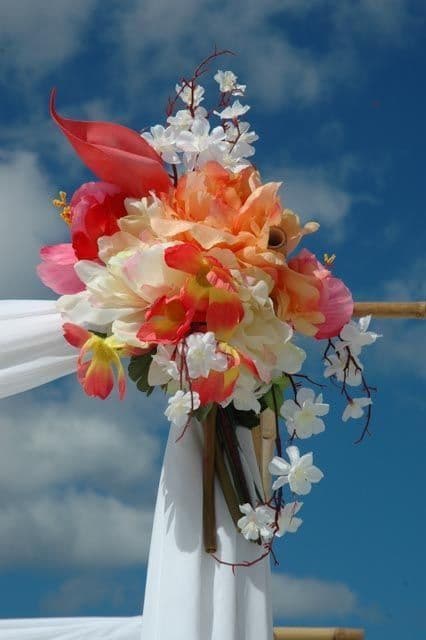 Wedding flowers, white and orange blooms with red accents, attached to white fabric, blue sky backdrop.