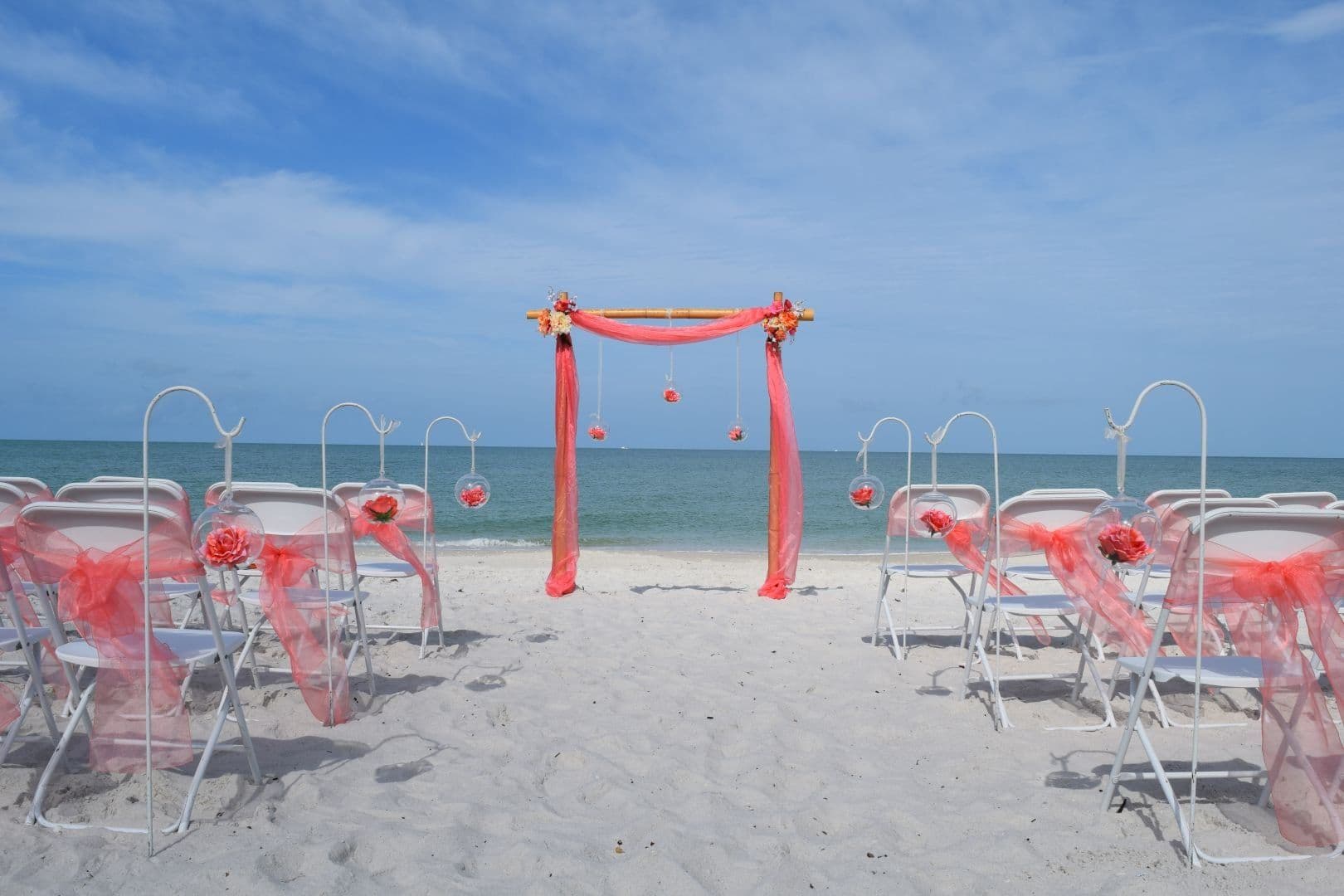 Wedding ceremony setup on a sandy beach with coral decor and ocean backdrop.