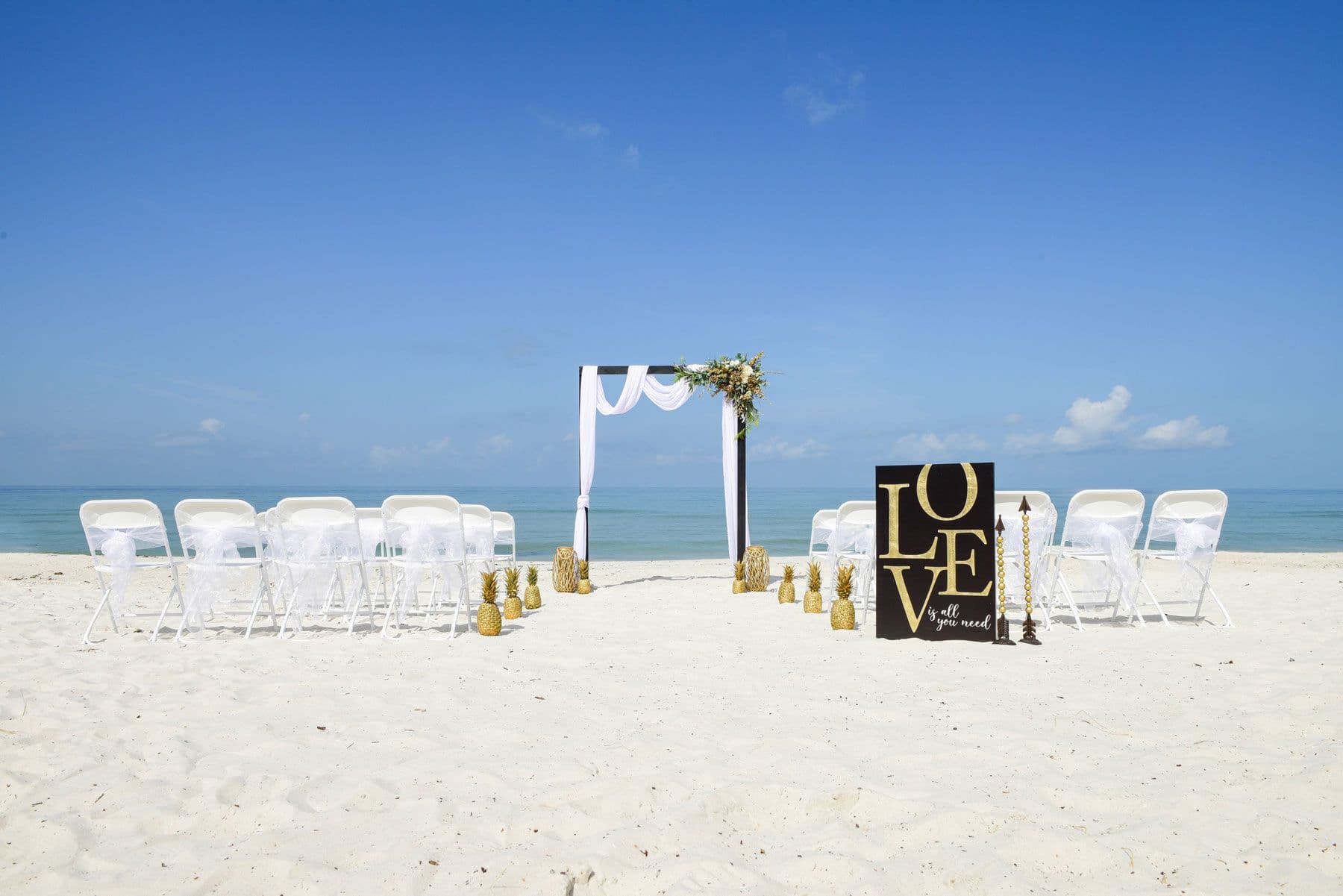 Beach wedding ceremony setup with white chairs, arch, and