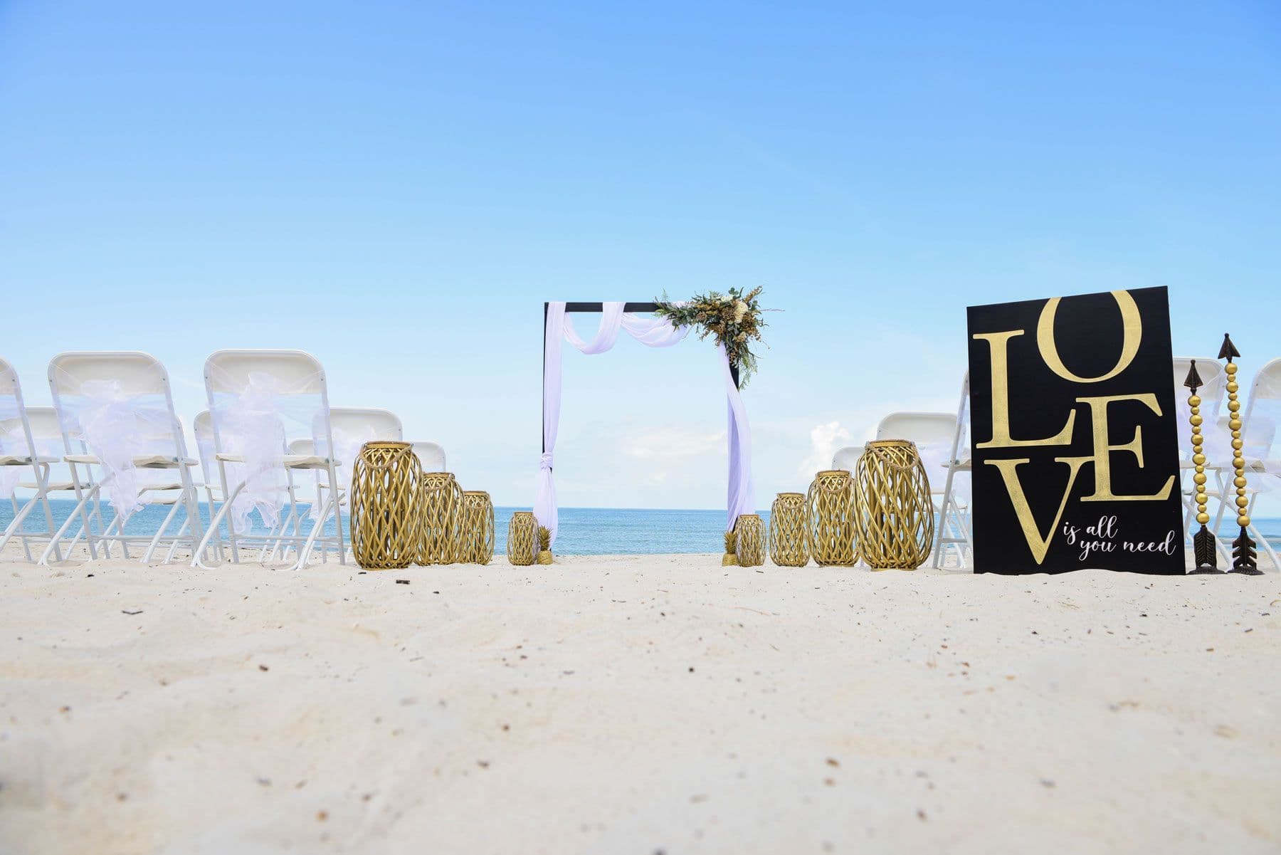 Beach wedding setup with chairs, an arch, and