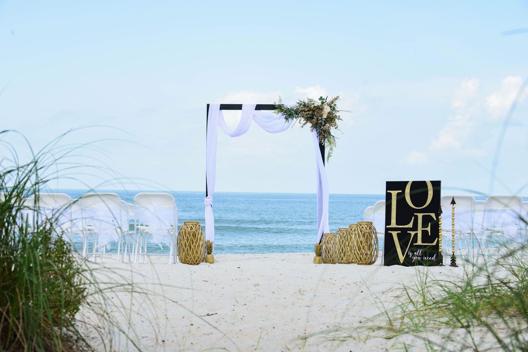 Beach wedding setup: white arch with draped fabric,