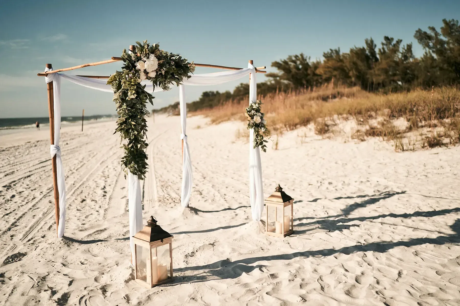 Wedding altar with draping fabric and floral accents on a sandy beach.