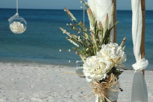 Wedding arch with white flowers on a sandy beach, ocean in background.